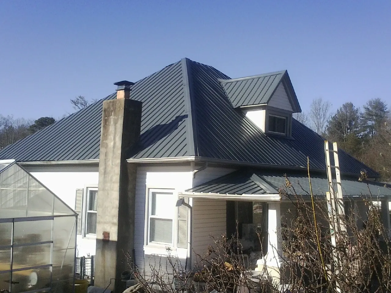 Dark blue standing seam metal roof on a white farmhouse with dormer — Slate & Tile Roof Repair by Roofing Brothers in Stromsburg