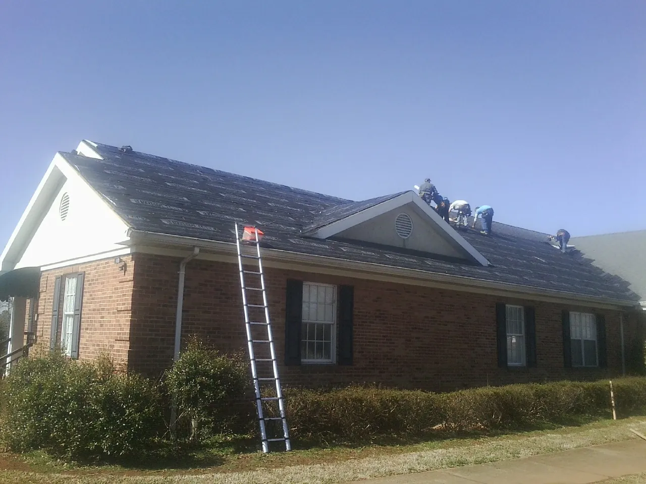 Crew tearing shingles off a brick ranch roof with a ladder set — Emergency Roof Repair work by our crew in Stromsburg
