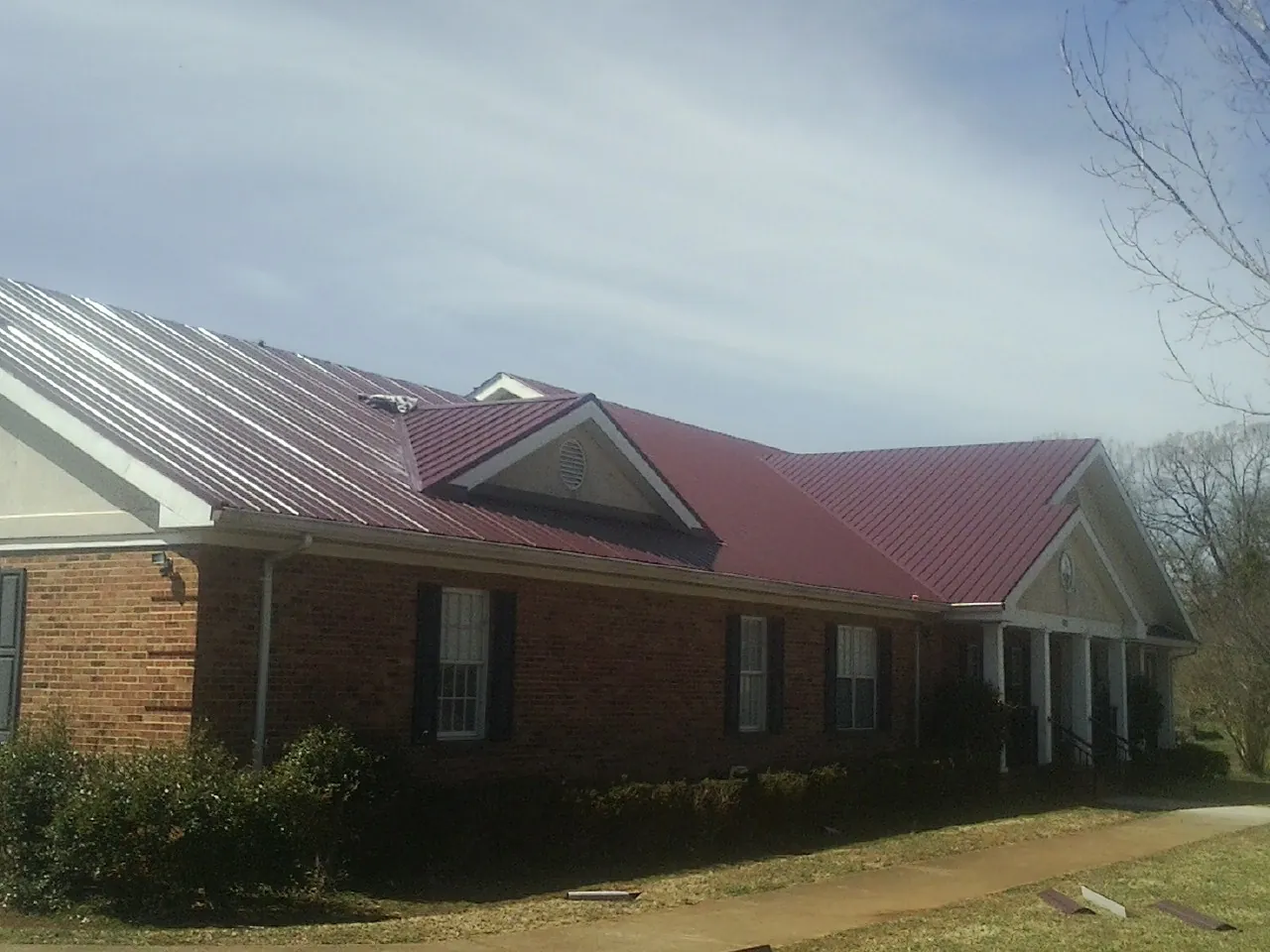 Red metal roof with gabled entries on a long brick building, from a Hail Damage Roof Repair job in Stromsburg