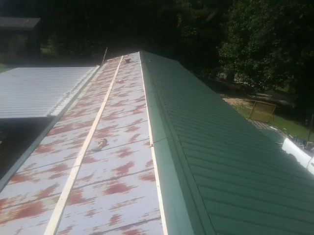 Old rusted panels beside newly installed green metal roofing — Wind Damage Roof Repair by Roofing Brothers in Stromsburg