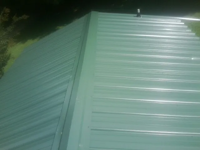 New green metal panels meeting at the ridge of a roof — Flat Roof Repair work by our crew in Stromsburg