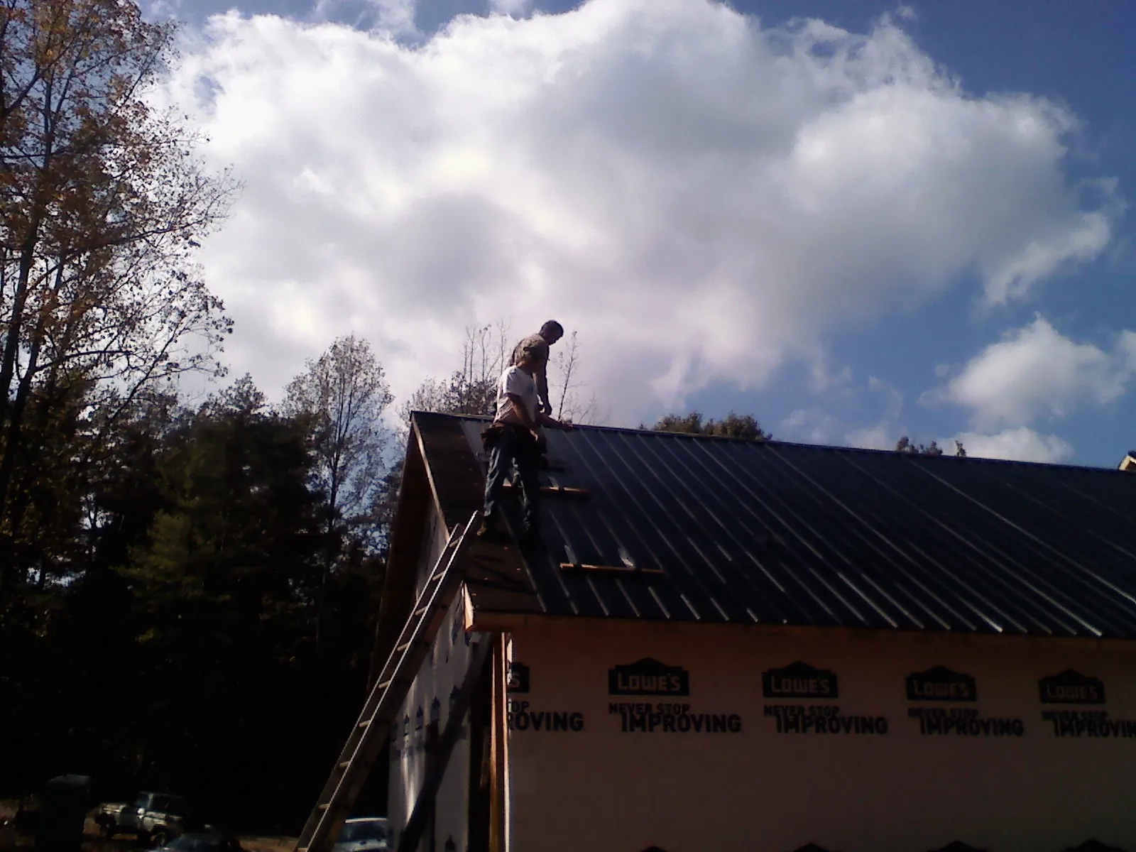 Roofer fastening dark metal panels high against a cloudy sky, from a Roof Inspection job in Stromsburg