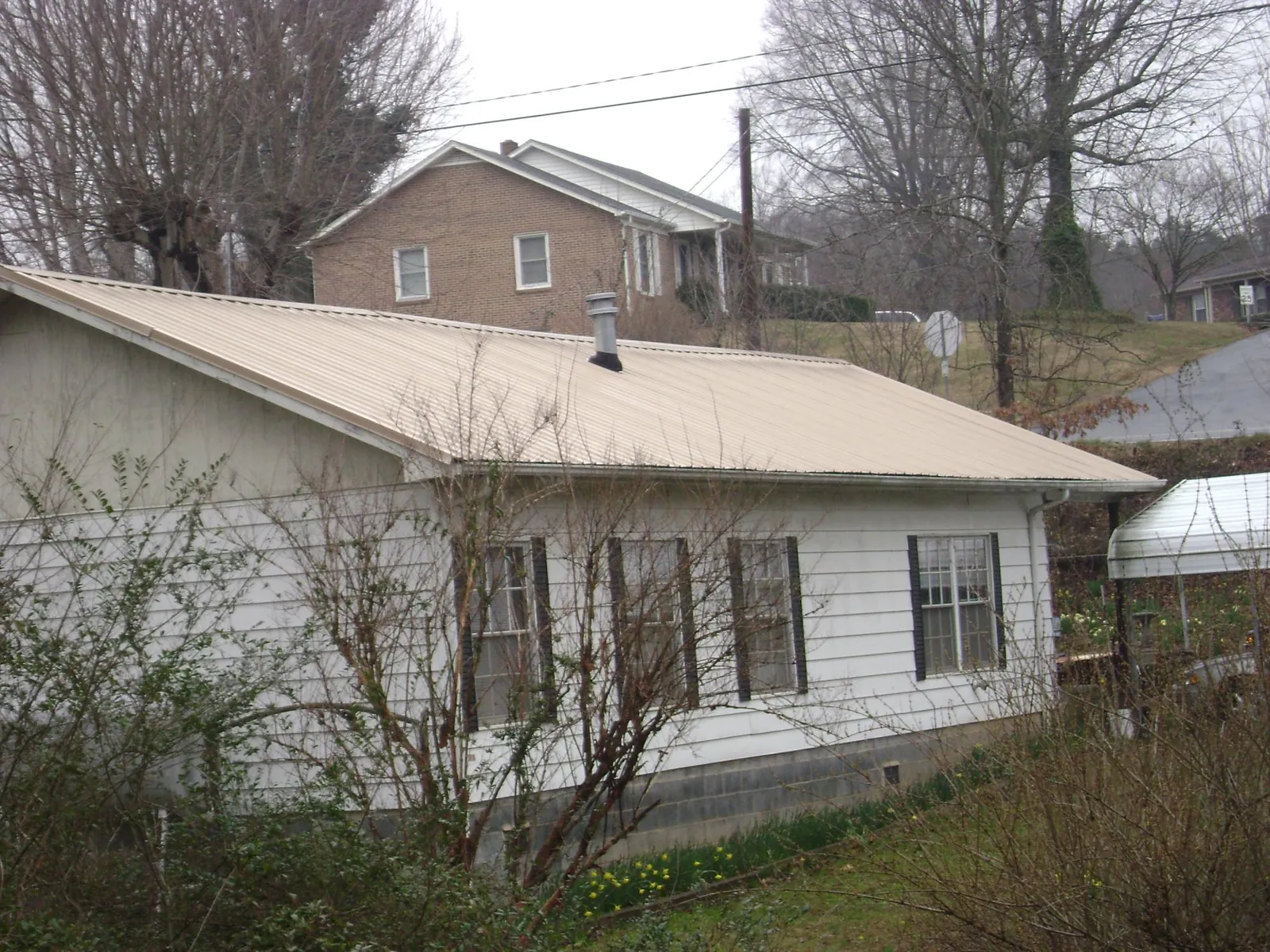 Tan metal roof on a white sided house set into a hillside — Commercial Roofing by Roofing Brothers in Stromsburg